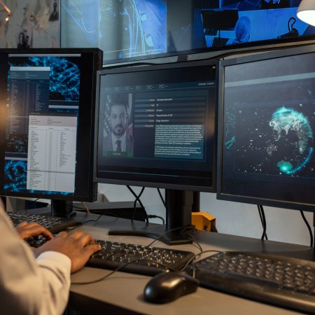 Young policeman entering personal data of suspect into computer database while sitting in front of monitors in office